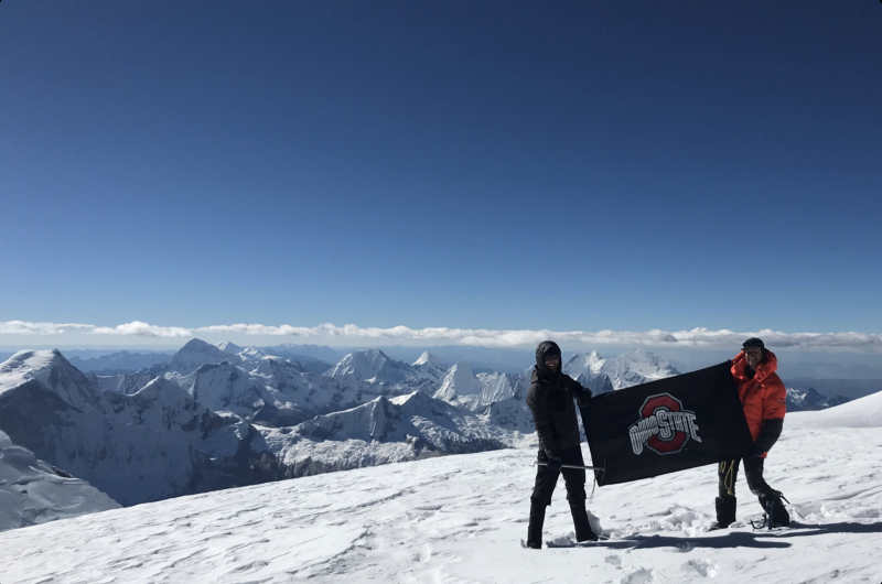 two students holding OSU flag on top of a mountain 